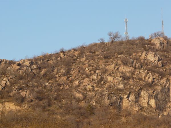 Landscape with jagged rock cliffs in brown tones and long, dry grass throughout.