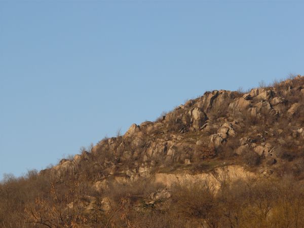 Landscape with jagged rock cliffs in brown tones and long, dry grass throughout.