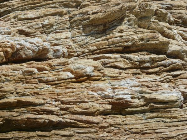 Rock cliff texture in brown and grey tones consisting of rough, layered rock.