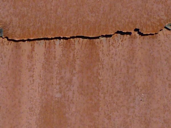 Roof texture consisting of dark red, rusting metal sheets with rotting edges.