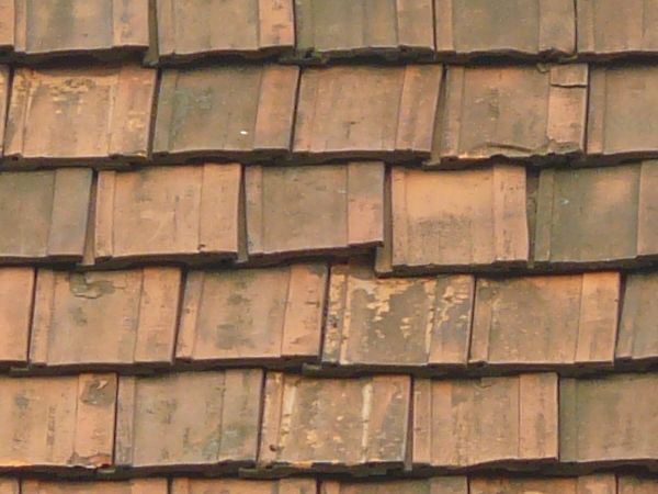 Old roof made of square, flat shingles in red and brown colors.