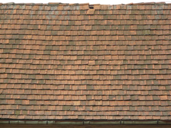 Old roof made of square, flat shingles in red and brown colors.