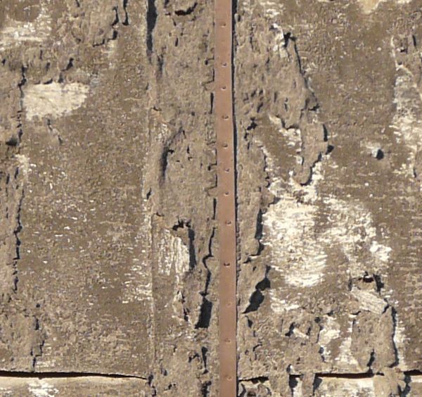 Texture of very worn roofing material nailed down with metal straps.