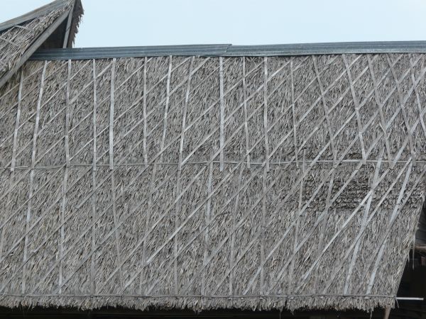 Old roof texture consisting of grey straw held down by wooden straps.