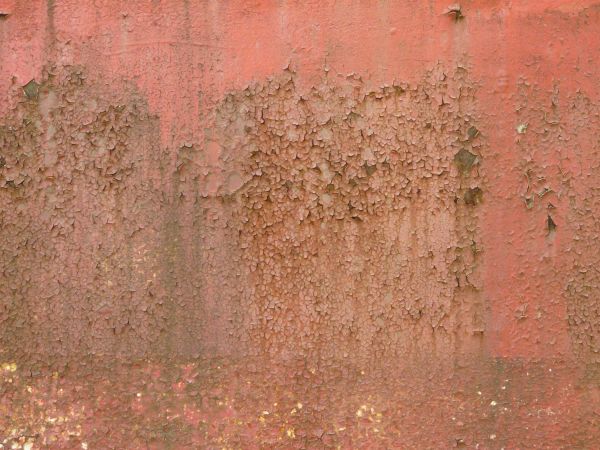 Chipping pink paint texture, covered with irregular brown and grey stains.