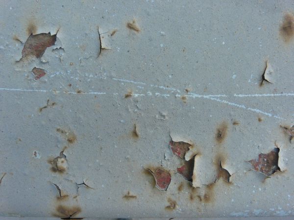 Grey painted metal texture, with small brown rust stains, and various chipping and cracking.