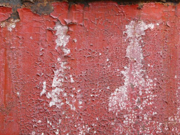 Chipping red paint texture, with an area of heavy rust visible underneath, and several white stains.