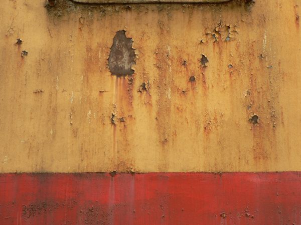 Red and white metal texture, with large chipping areas and completely covered by orange and brown rust stains.
