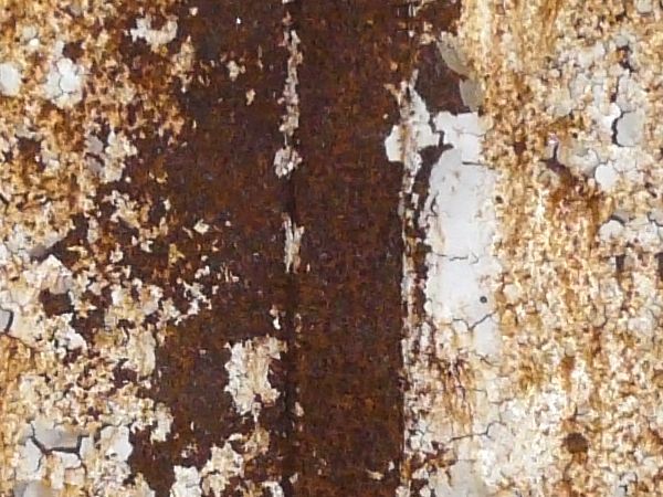 Heavily rusted metal texture, with large areas of chipping and darkly stained white paint.