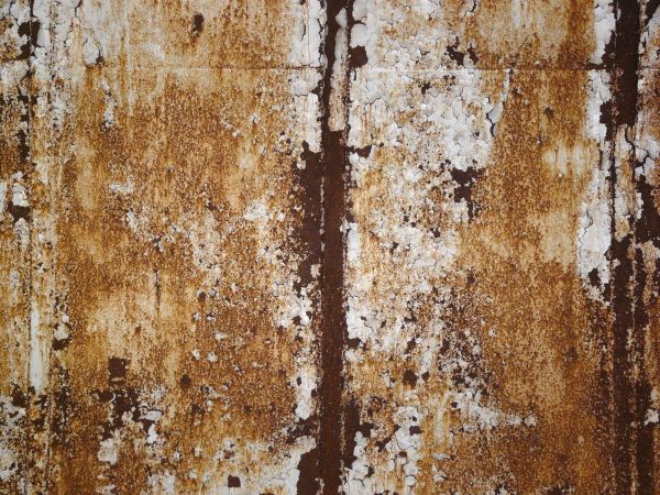 Heavily rusted metal texture, with large areas of chipping and darkly stained white paint.