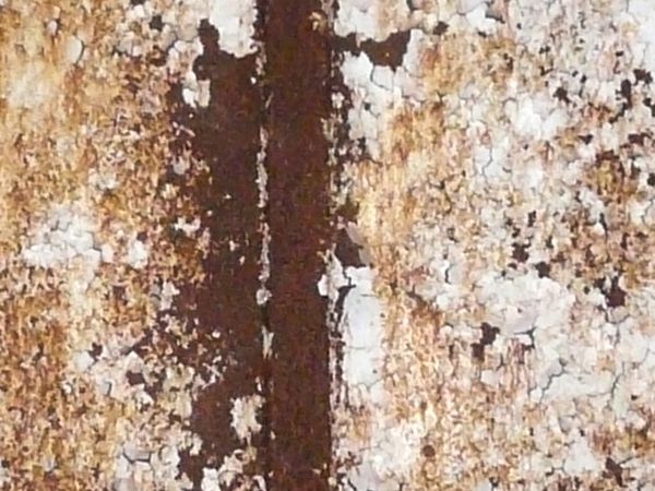 Heavily rusted metal texture, with large areas of chipping and darkly stained white paint.