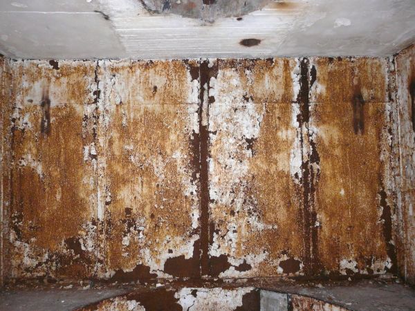 Heavily rusted metal texture, with large areas of chipping and darkly stained white paint.