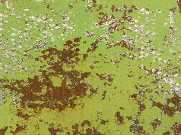 Rusted metal texture, covered by a chipping surface of lime green paint with extensive white staining.