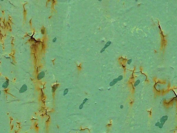 Light green metal texture, with small cracks and brown rust stains visible throughout.