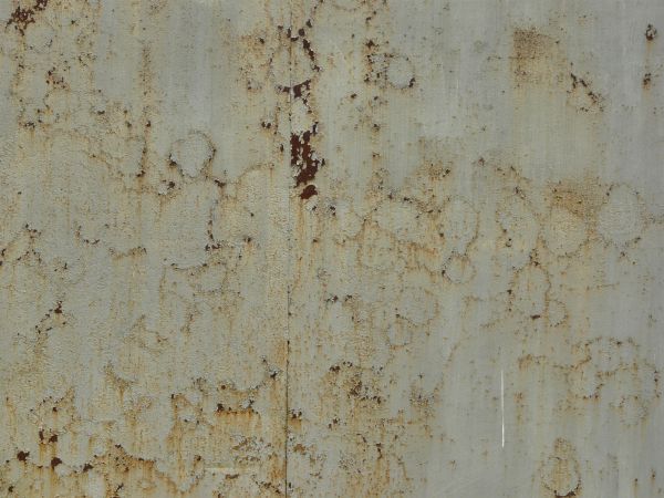 Small rust spots texture, present on a coarse surface of white paint. Faint brown staining is also visible.