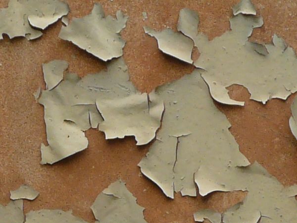 Tan painted metal texture with extensive chipping and peeling, and a surface of rusted metal visible underneath.