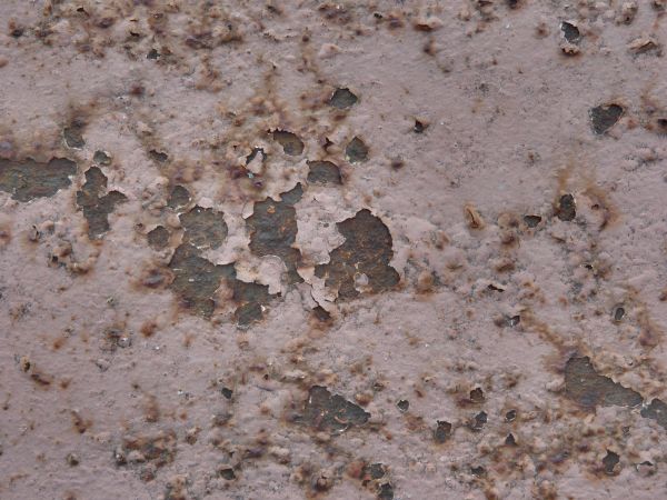 Pink painted metal texture, with several large chipped areas and heavy rust visible beneath.