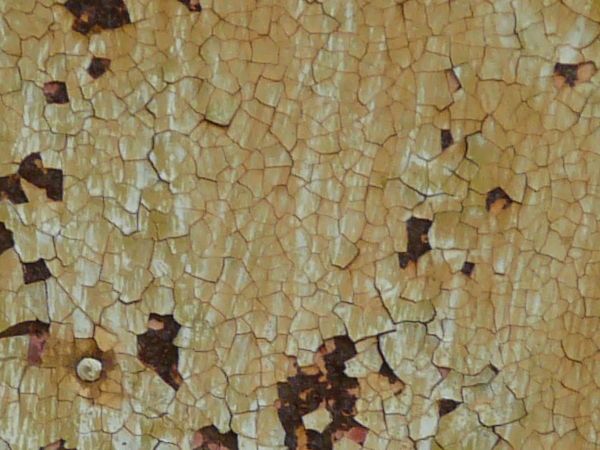 Metal texture with extensive cracking in the white and yellow paint, and areas of dark red rust visible underneath.