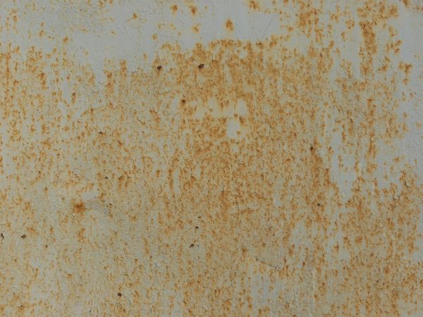 White metal texture covered with many faint cracks, rust patches and large areas of light brown staining.