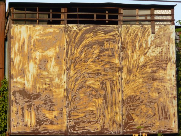 Yellow and brown rust texture, formed in a swirling pattern on three panels of white painted metal.