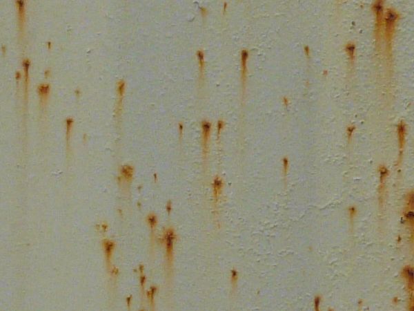 Orange rust marks texture, scattered over a surface of white metal. Large stains and completely rusted patches are also visible.