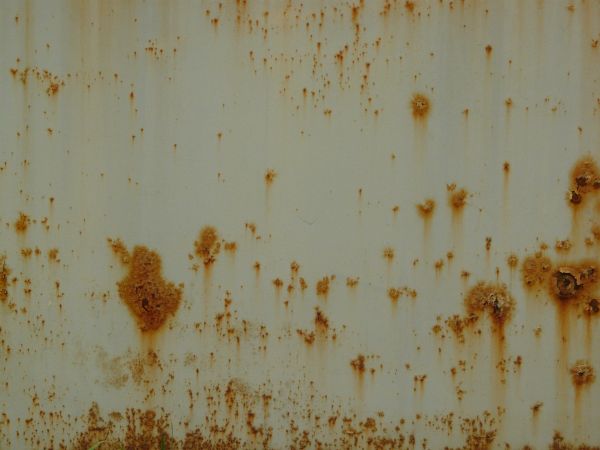 Orange rust marks texture, scattered over a surface of white metal. Large stains and completely rusted patches are also visible.