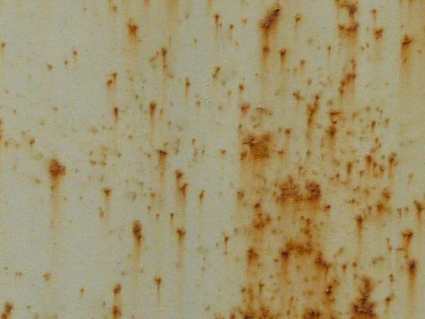 Orange rust scratches texture, spread irregularly in small marks and patches on a stained surface of white metal.