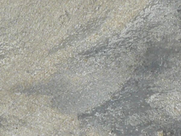 Texture of smooth, dark grey soil, with irregular windswept patterns of tan soil across its surface.