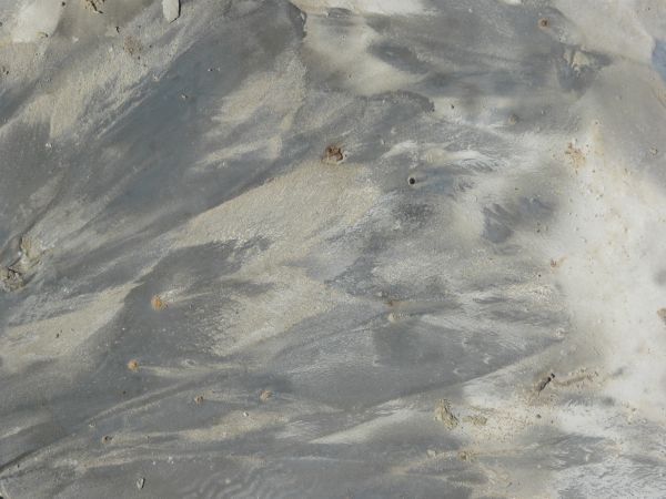 Texture of smooth, dark grey soil, with irregular windswept patterns of tan soil across its surface.