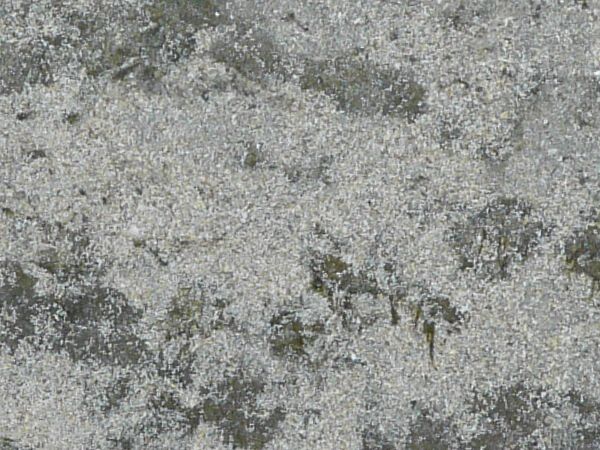 Rocky grey soil texture, covered irregularly by a thin layer of white sand.