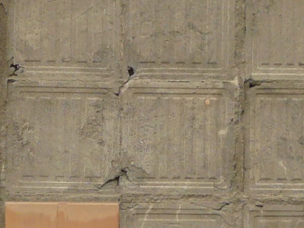 Texture of square brown-orange tiles partially covering deteriorating mortar wall with imprinted pattern.