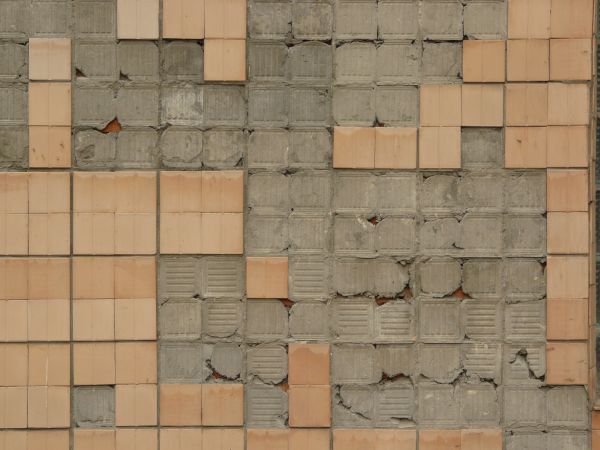 Texture of square brown-orange tiles partially covering deteriorating mortar wall with imprinted pattern.