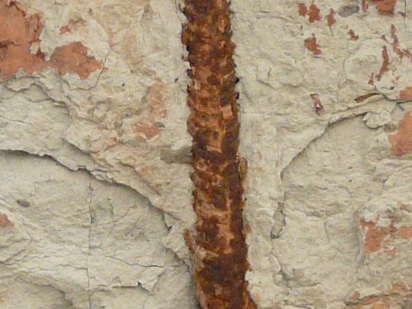 Texture of rusted metal wire in front of a stained uneven concrete surface.