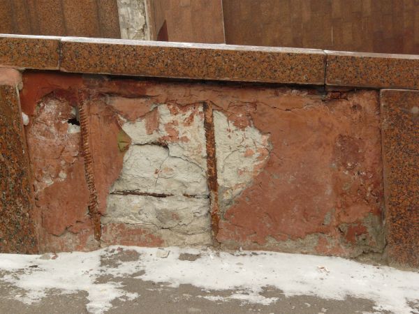 Texture of rusted metal wire in front of a stained uneven concrete surface.