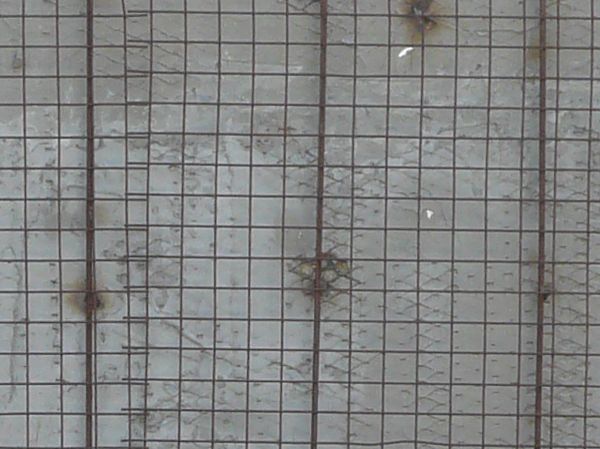 Texture of grid patterned fence over a stained gray concrete wall.