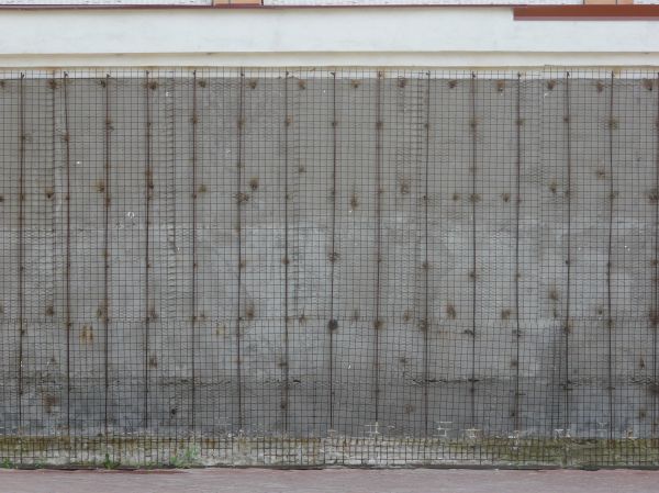 Texture of grid patterned fence over a stained gray concrete wall.