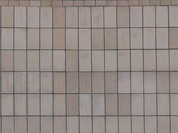 Small, rectangular tiles in light pink tone set evenly with slightly worn, dirty surface.