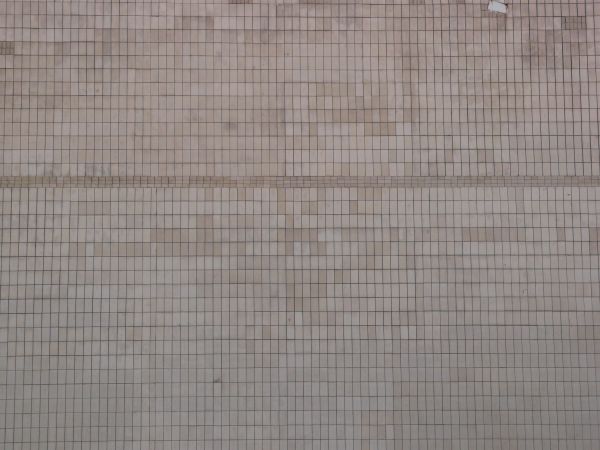 Small, rectangular tiles in light pink tone set evenly with slightly worn, dirty surface.
