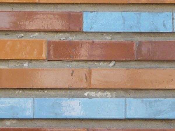 Seamless texture of long, narrow tiles in red tones with blue tiles placed randomly.