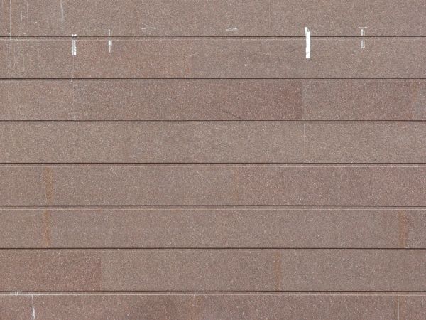 Siding of long tiles in dark red tone with horizontal seams and slightly dirty surface.