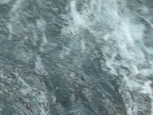 Dark water texture with rough surface and some white foam.
