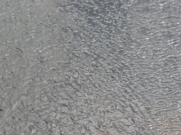 Water texture with small waves and very shiny, grey surface.