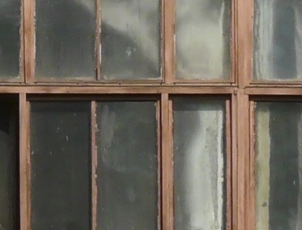 Small brown windows texture set in long rows, separated by sections of yellow stone wall. Various boards, wires and dark surfaces are visible inside, and several panes are missing or broken.