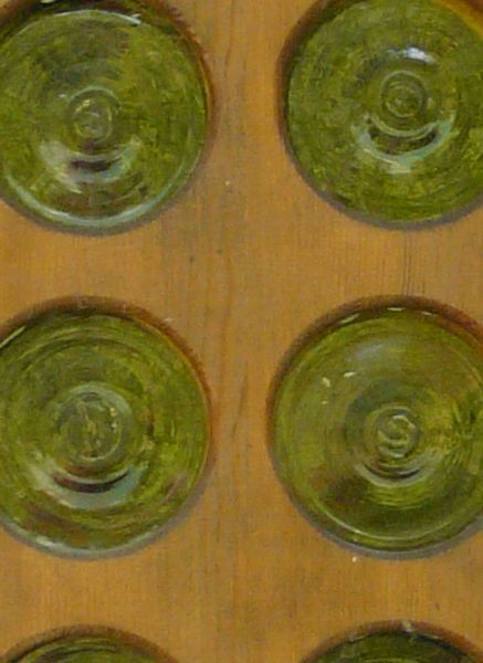 Green window texture, made up of small, separated circular panes, set in a large frame of smooth wood. Various patterns and tracery run along the top of the frame.