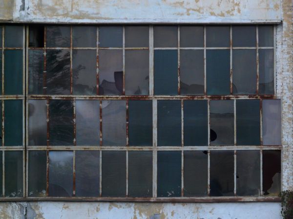 Reflective windows texture separated by rusting white trim and surrounded by a whitewashed stone wall. The panes have blue and green tints, and several of them are broken.