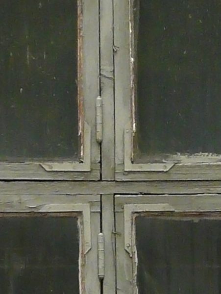 Grey windows texture with rough chipping paint on the trim and tan brick surrounding them. A metal grid is faintly visible inside, and various paint marks are on the glass.