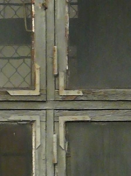 Grey windows texture with rough chipping paint on the trim and tan brick surrounding them. A metal grid is faintly visible inside, and various paint marks are on the glass.