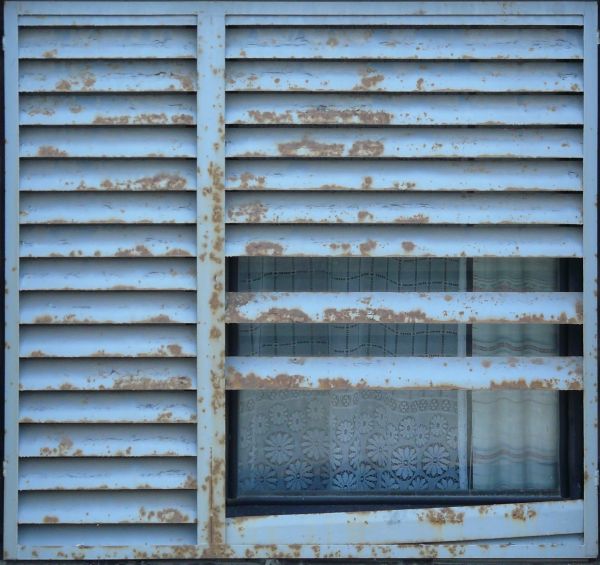 Blue window texture made up of two sections of wide metal shutter blades with rusted patches.