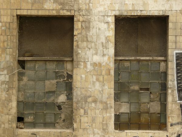 Glass brick windows texture, with several holes and broken areas, and large clouded panes set over the bricks. The windows are set in a wall of stained yellow brick.