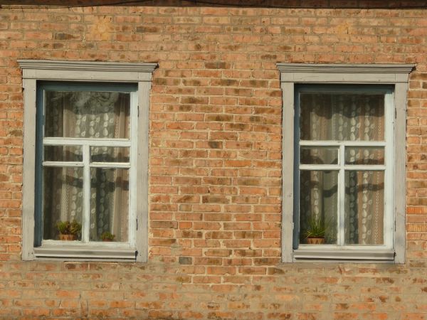 Grey windows texture, set in a red and brown brick wall, with white lace curtains visible behind the glass.